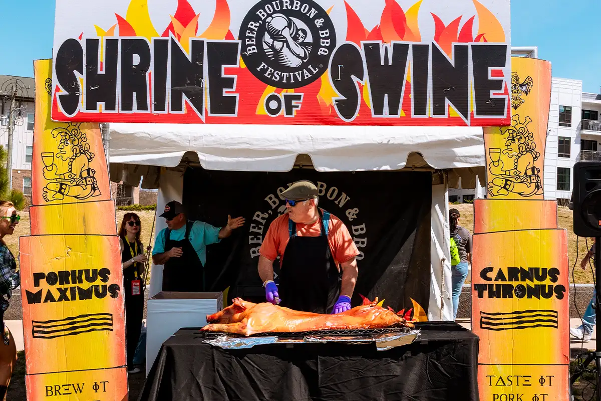 a man stands at a Shrine of Swine stand at tha Beer, Bourbon & BBQ Festival