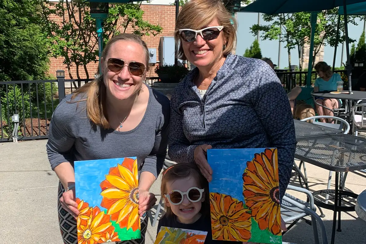 two adults and a child post with their paintings