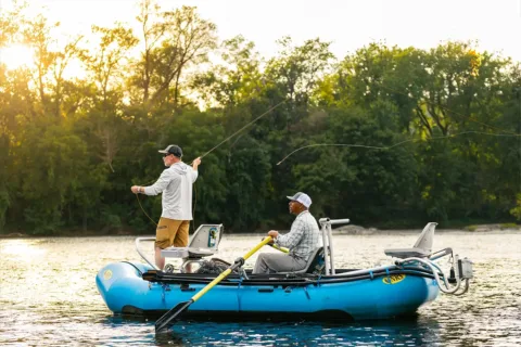 two men in a boat with one holding the oars and another fly fishing
