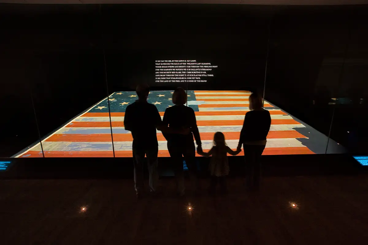a family stands in front of a large American flag that's part of the America 250 exhibit at Smithsonian’s National Museum of American History