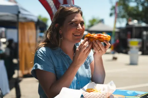a woman at a picnic table holds a piece of pizza