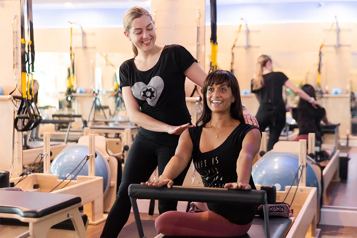 Instructor helping woman doing reformer pilates at Club Pilates