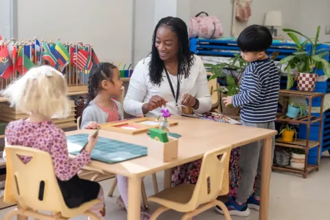 a teacher sits at a table in a kindergarten classroom