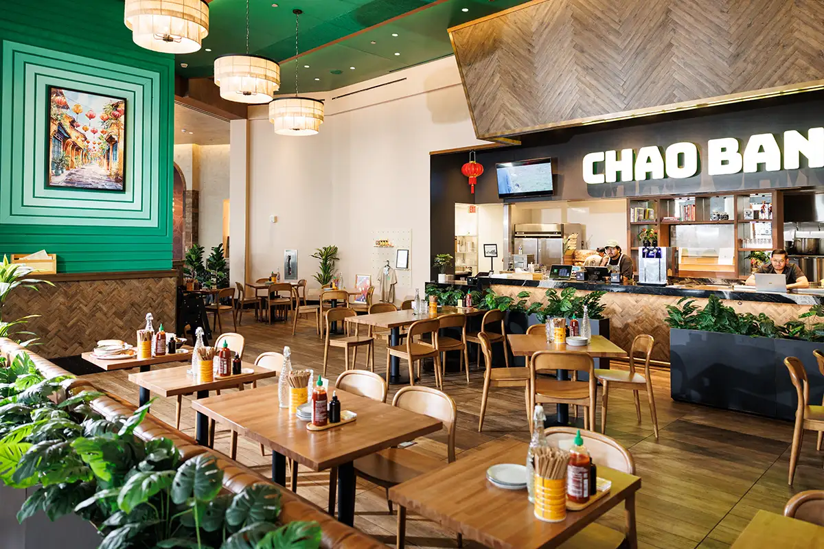 Interior of Chao Ban restaurant with wooden tables and chairs, green accent wall and ceiling, and order counter.