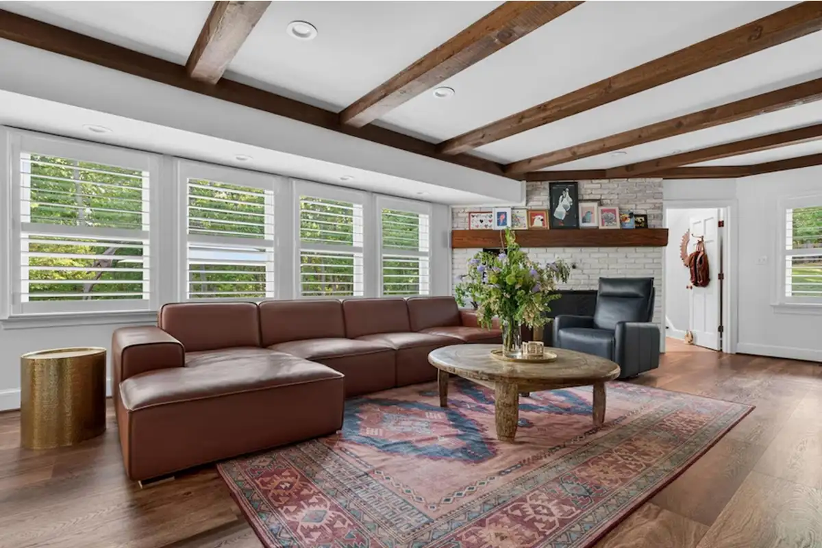 Living room with exposed wooden beam ceiling, white brick fireplace, and large windows of 3204 Mountain Rd