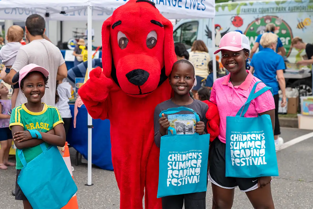 kids stand with Clifford the Big Red Dog holding Summer Reading program tote bags
