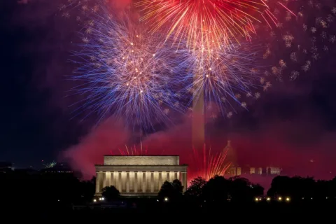 Fireworks exploding over the Potomac river with Kennedy Center, Monument, and Capital in the background