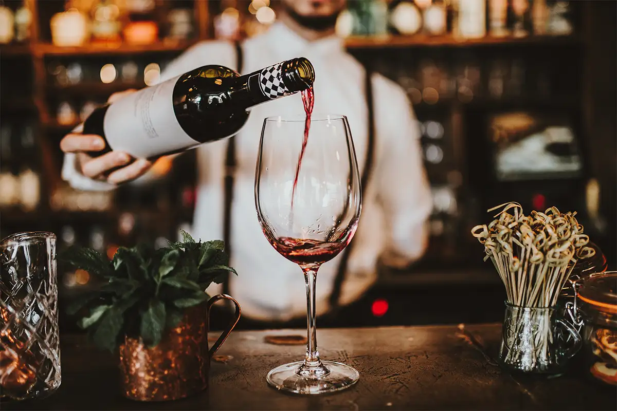 a bartender pours a glass of red wine