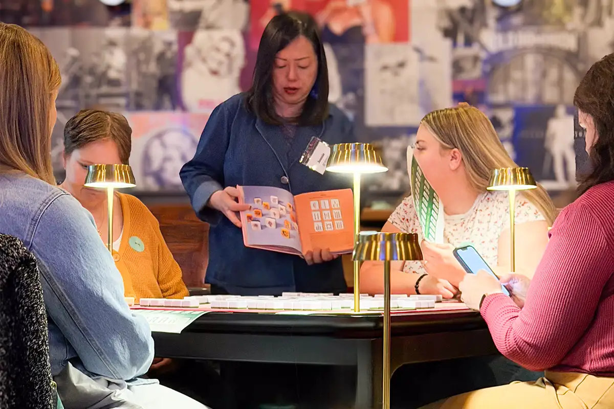 Jennie Mak instructing mahjong from book to table of women