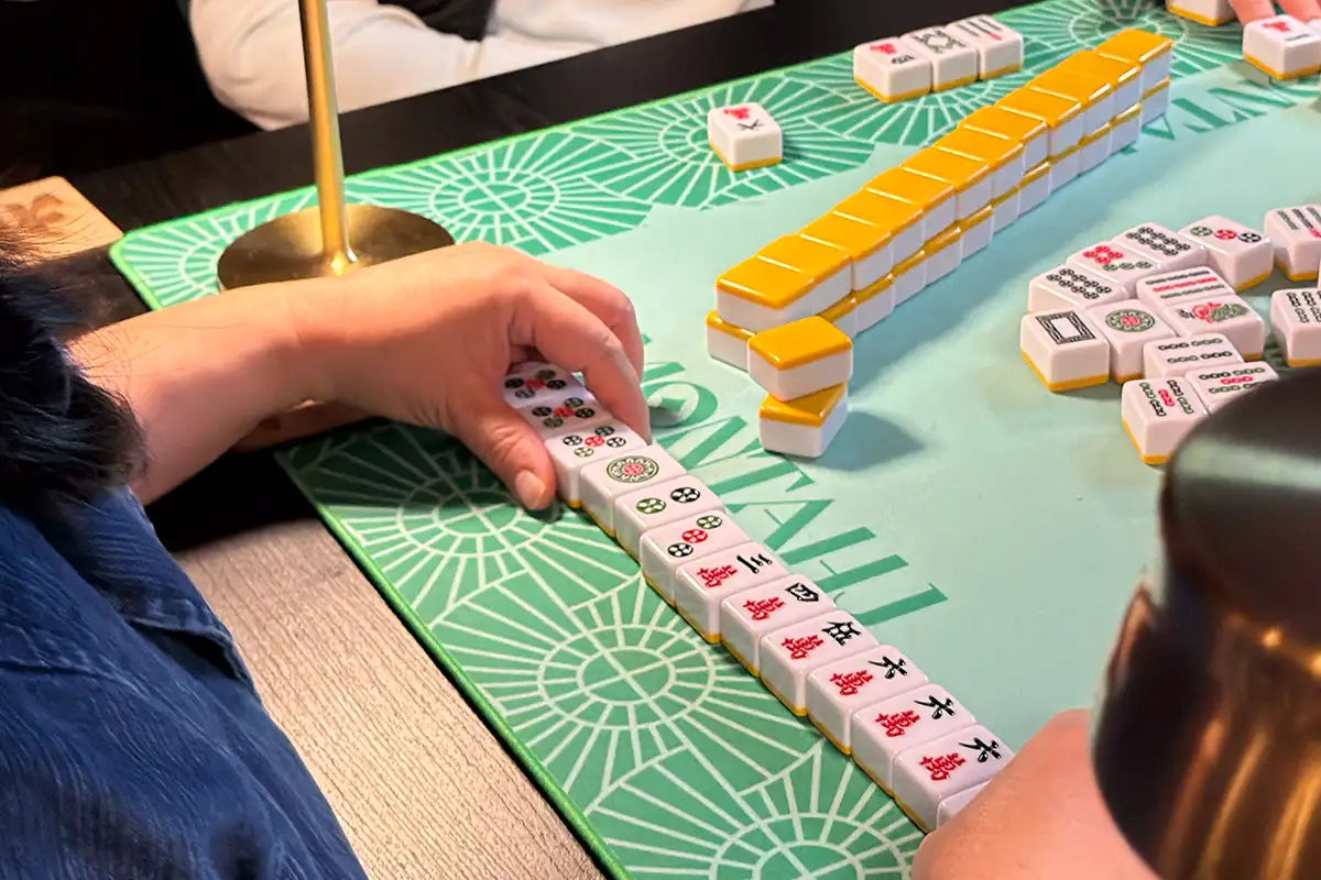Close up of person playing and mahjong board and tiles