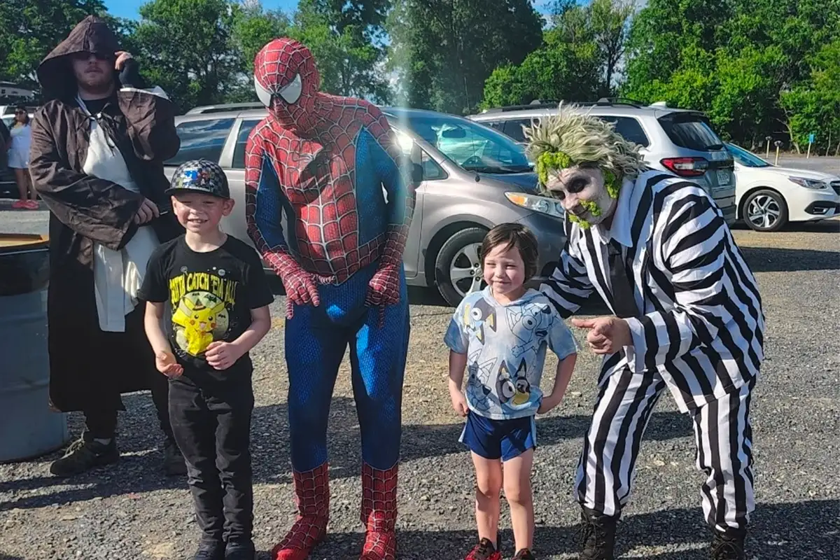 Kids posing with community members dressed as movie characters (Spiderman, The Joker, Obi-Wan Kenobi)