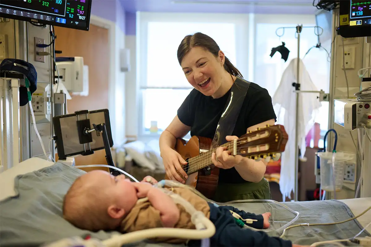 Woman playing guitar and singing to baby in hospital bed