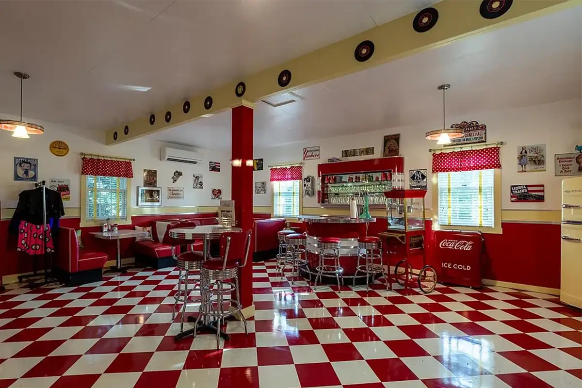 Redesigned retro diner garage with red accents, checkered flooring, and booths, tables, and chairs of 2525 Gibson Ct