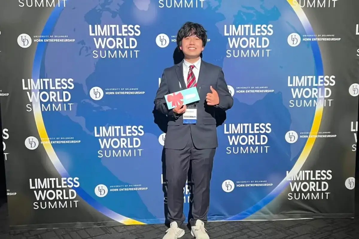 Chantilly High School student Brendan Li stands in a suit in front of the Limitless World Summit background