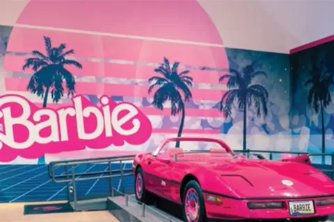 A pink Barbie convertible in front of a Barbie sign