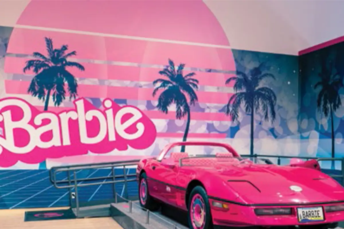 A pink Barbie convertible in front of a Barbie sign