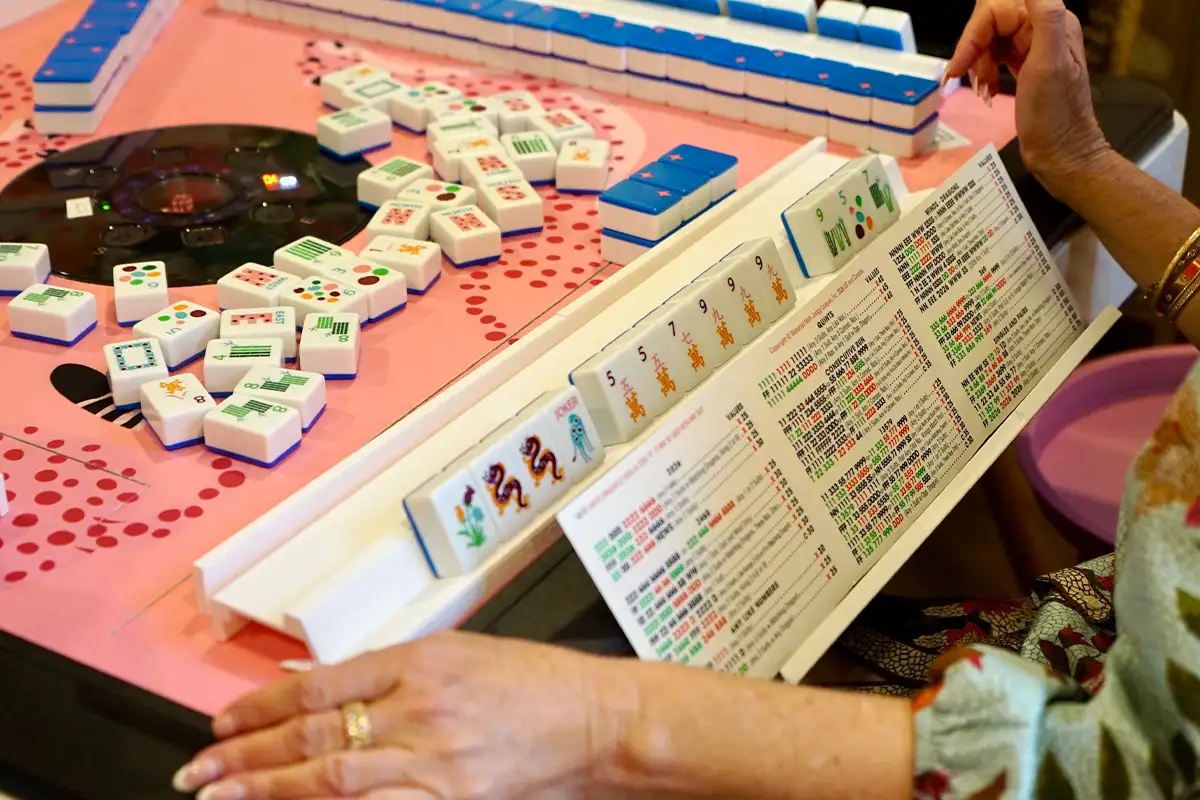 a woman looks at her mahjong card with a board and tiles in the background