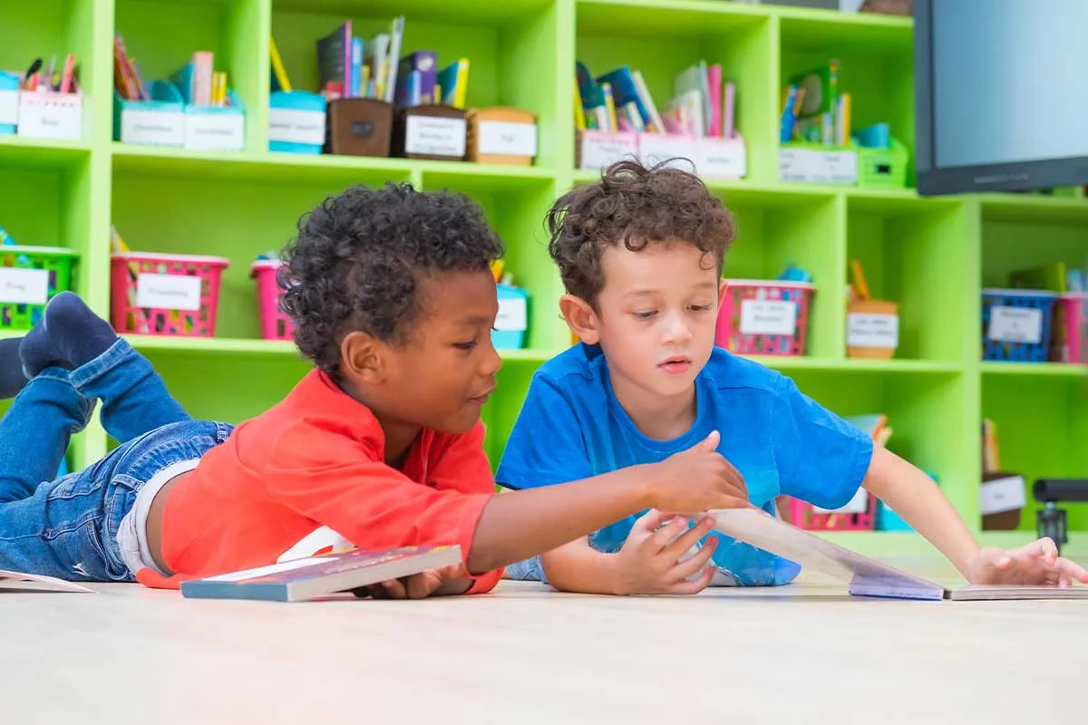 two toddler boys reading books on the floor