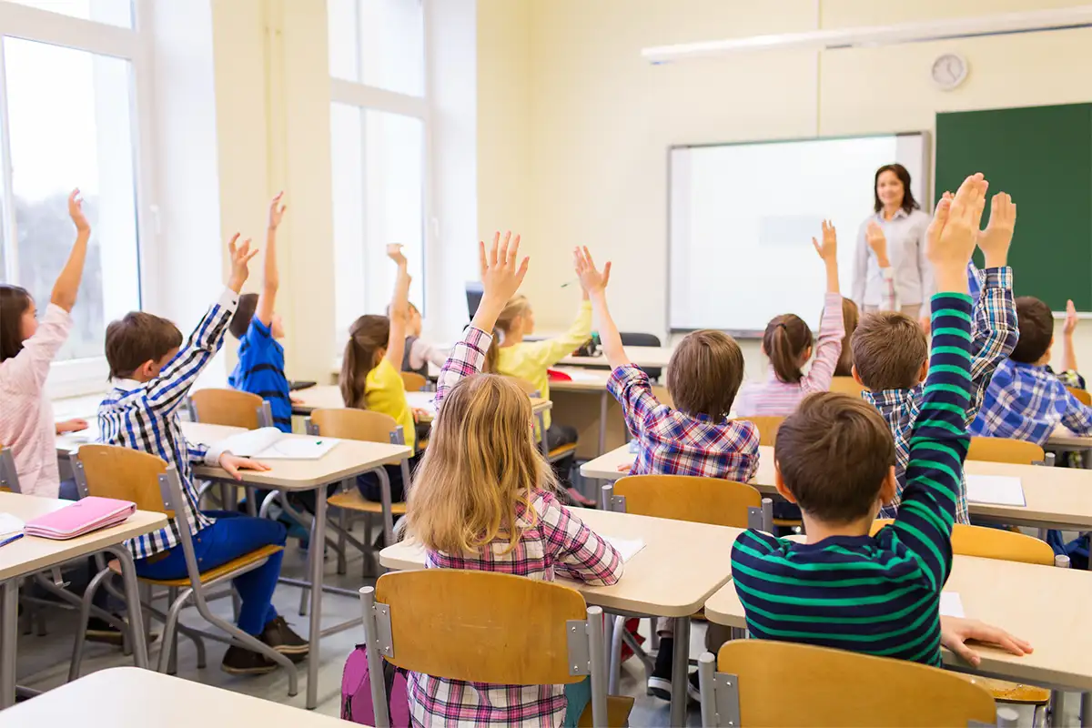 elementary school kids raise their hands in a classroom