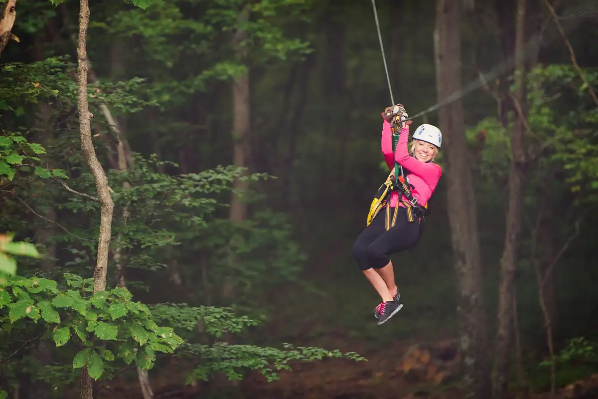a woman in a pink top ziplines through the trees