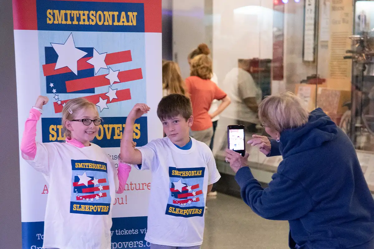 two kids pose in front of a Smithsonian Sleepovers sign