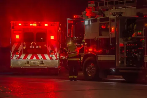 an ambulance and fire truck parked on a road at night with a firefighter getting in the firetruck