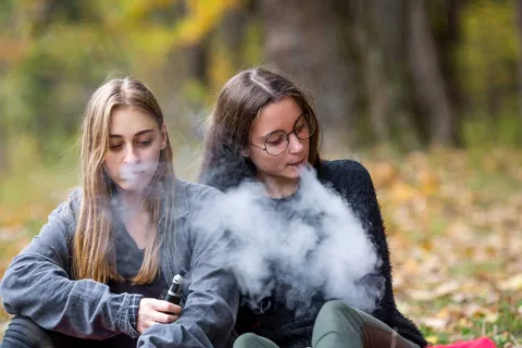 two teens vaping while sitting outside