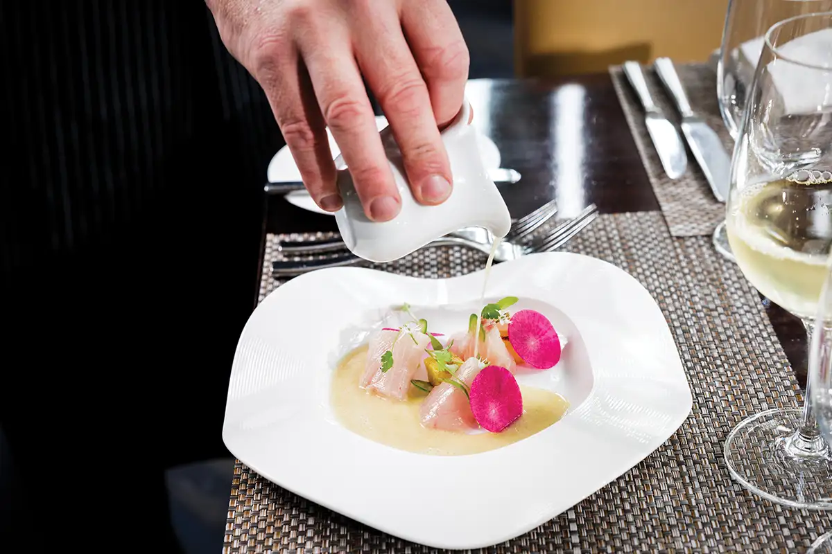 person pouring sauce over fish dish