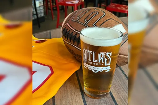 Atlas Brew Works draft beer glass in front of football