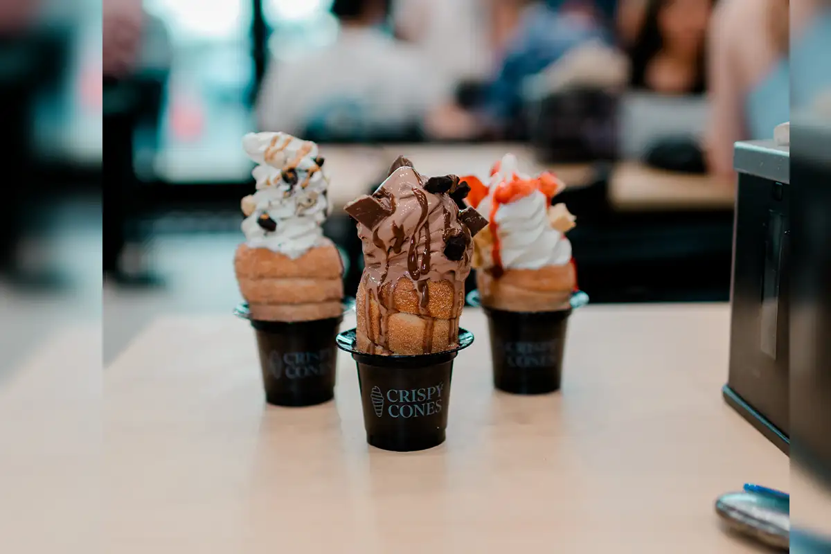 Three ice cream sundaes in edible cake cones and cups on counter