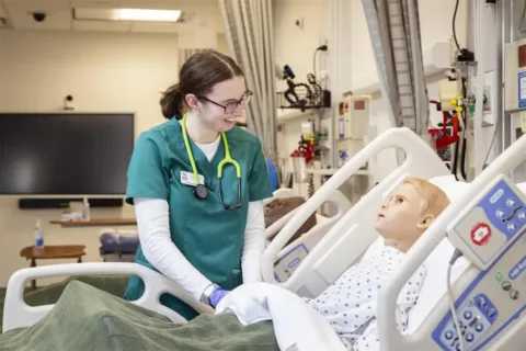 Photo of Nursing Student practicing on a test dummy in a hopsital bed