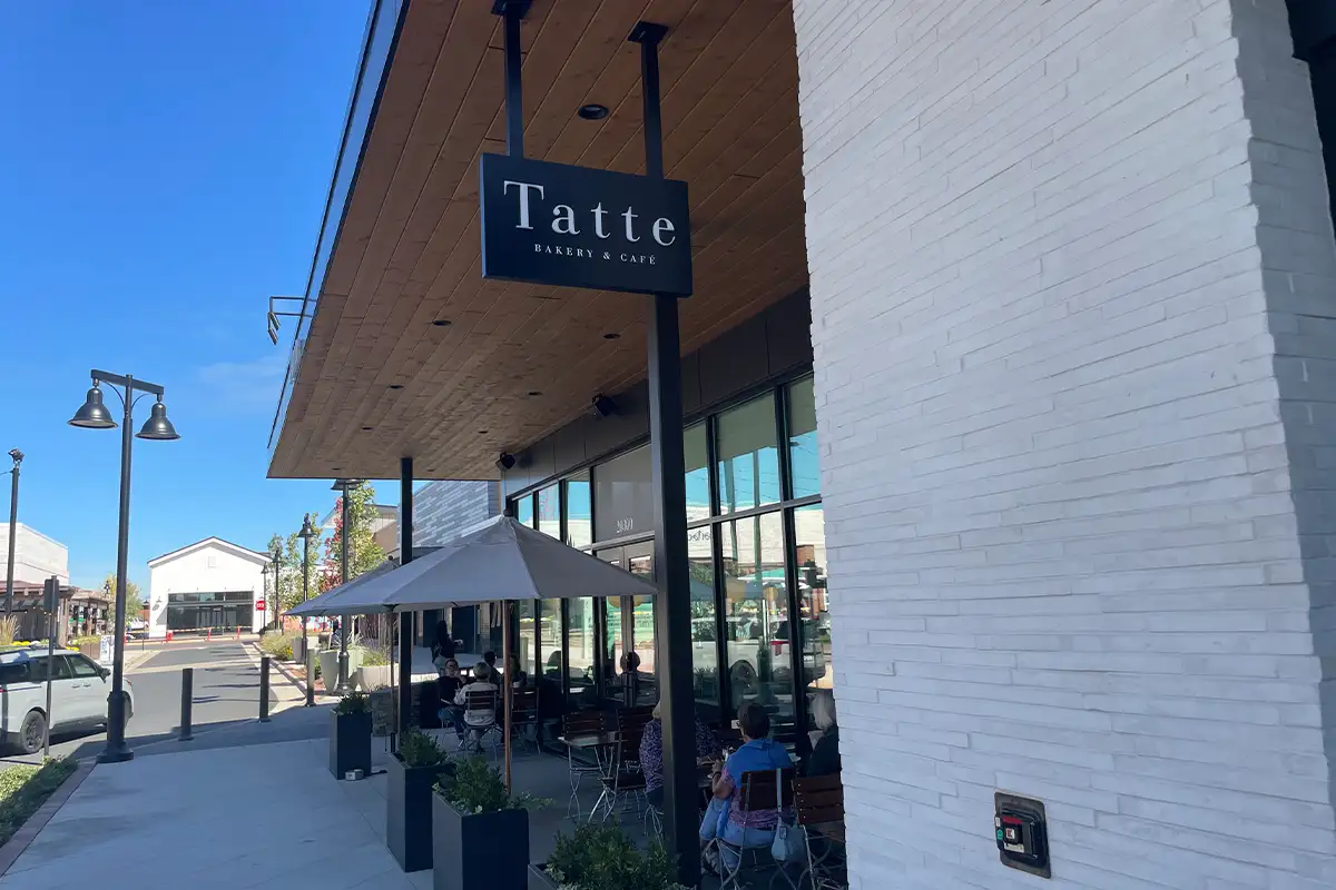 Photo of Tatte bakery store sign hanging from a wooden extended roof over the bakery's outdoor front patio
