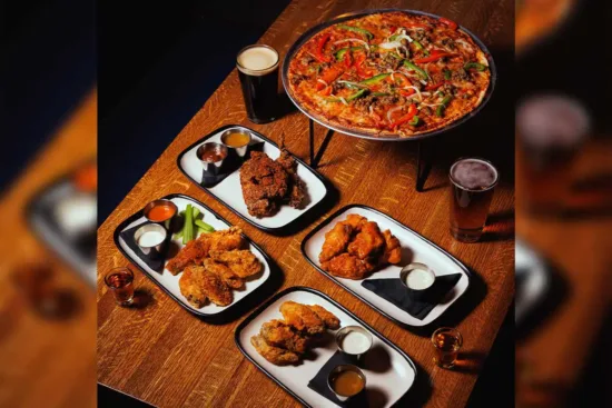 Four chicken wing platters in front of a bell pepper pizza